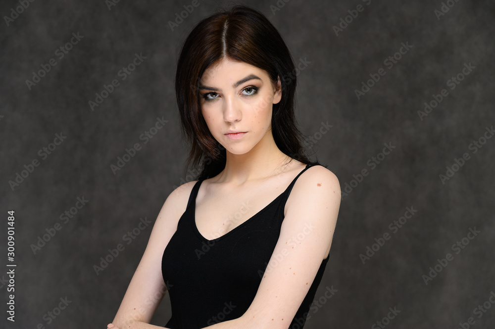 Close-up portrait of a young pretty girl student with long black hair, on a gray background. He stands right in front of the camera, showing his hands in different poses with different emotions. Close-up portrait of a young pretty girl student with long black hair, on a gray background. He stands right in front of the camera, showing his hands in different poses with different emotions.