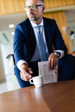 selective focus of handsome businessman in suit and glasses taking cup