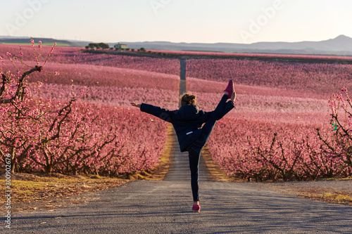 Young girl doing a gymnastic pirouette with the pink sea of peaches trees in bloom as background. Aiton alndscape photo