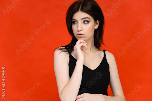 Close-up portrait of a young pretty girl student with long black hair, on a red background. He stands right in front of the camera, showing his hands in different poses with different emotions.