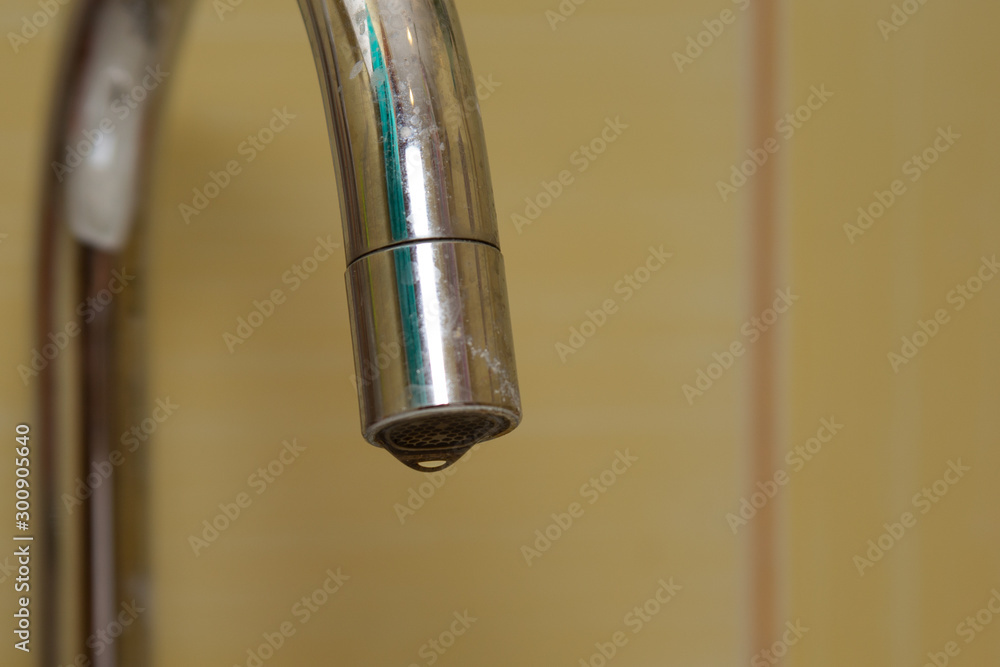 A drop of water is leaking from the tap. The loss of water due to poor plumbing. Environmental problem-loss (lack) of drinking water. A drop of water is leaking from the tap. The loss of water due to poor plumbing. Environmental problem-loss (lack) of drinking water.