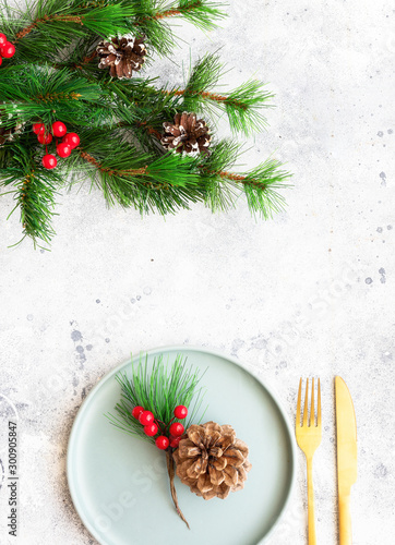 Christmas celebration background. Green plate fir tree brunch and golden cutlery. Winter holidays and festive dinner concept. Copy space.