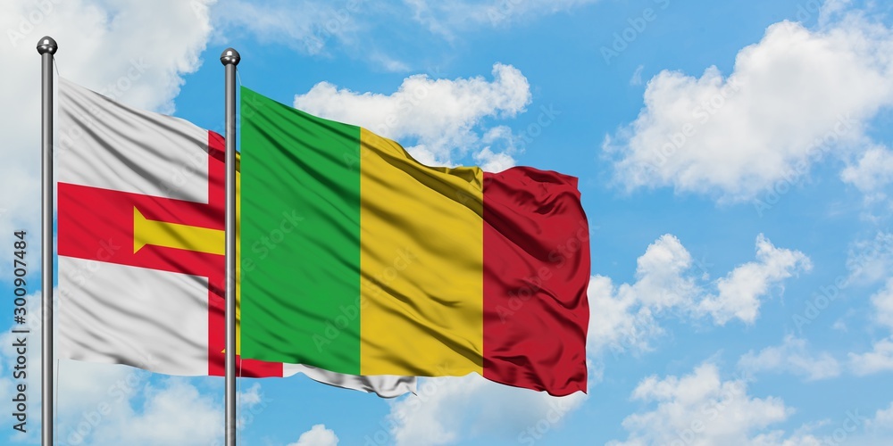 Guernsey and Mali flag waving in the wind against white cloudy blue sky together. Diplomacy concept, international relations.