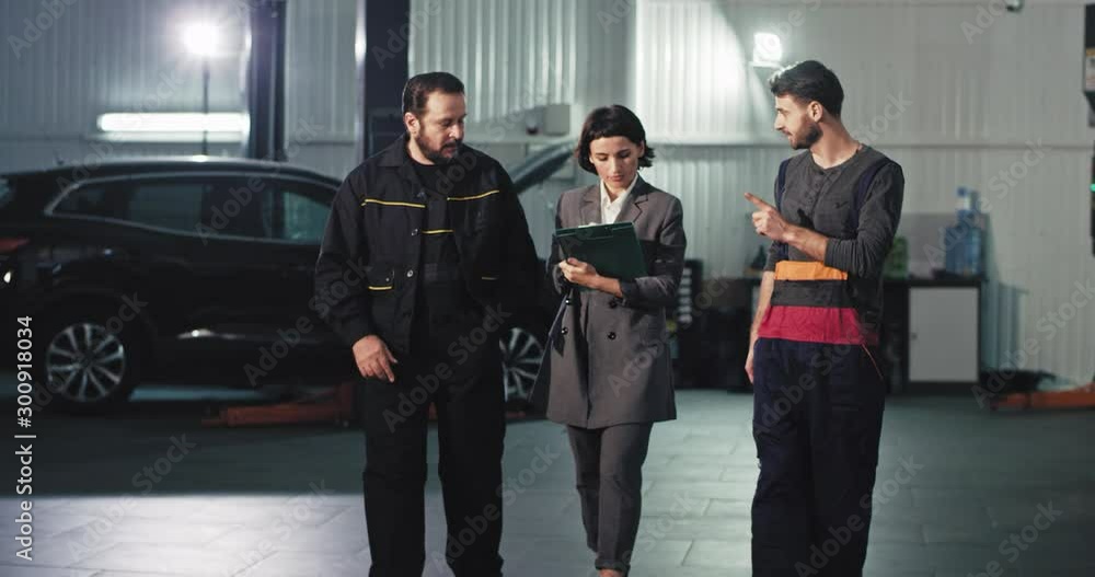 In front of the camera auto service team woman main manager and two mechanic analyzing the plan of work concentrated they have a conversation In front of the camera auto service team woman main manager and two mechanic analyzing the plan of work concentrated they have a conversation