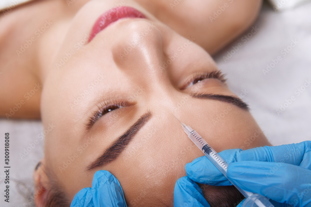 Closeup Portrait of young Caucasian woman getting cosmetic injection of botox in forehead. People, cosmetology, plastic surgery and beauty concept.