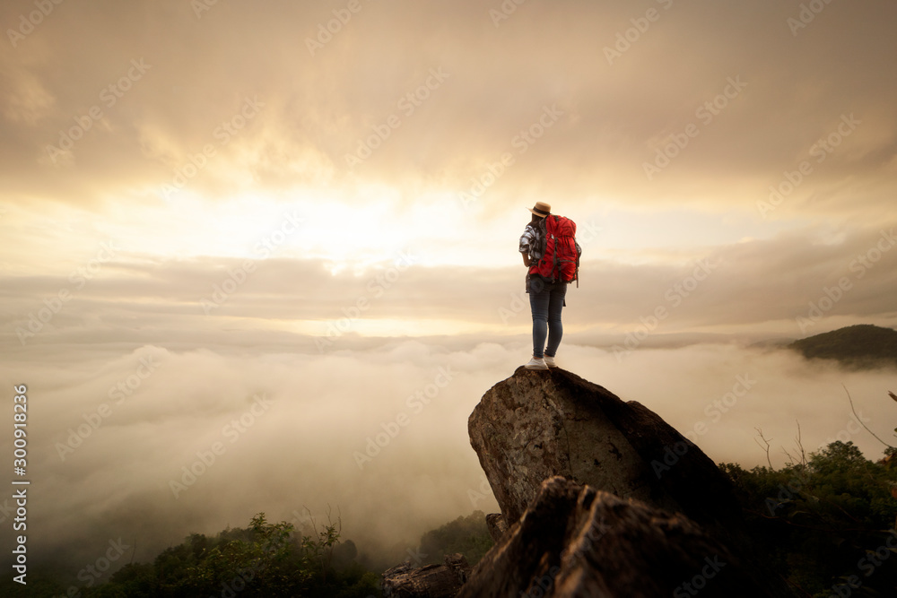 Backpacker woman raise hand up on top of mountain with sun sky and fog backgeound