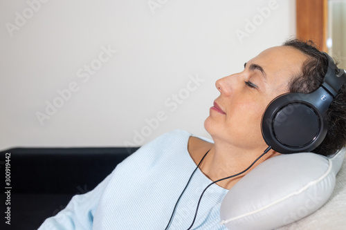 Young Spanish woman listening to music at home with headphones