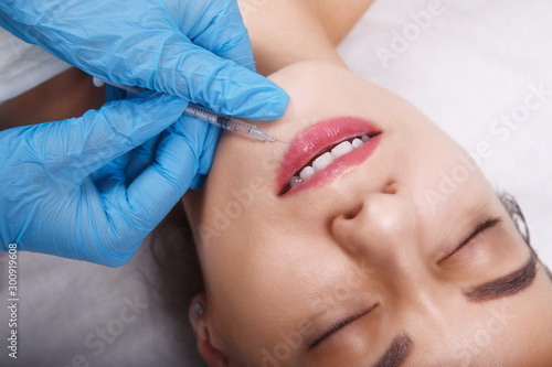 Facial Beauty Injections. Portrait Beautiful Young Woman Receiving Hyaluronic Acid Injection. Closeup Of Hands In Gloves Holding Syringe Near Attractive Female Face.