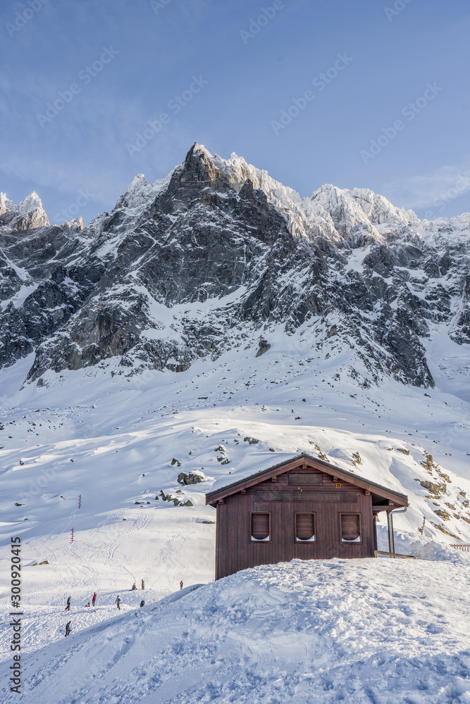 Dark wooden house on snow slope before Aiguille du Plan