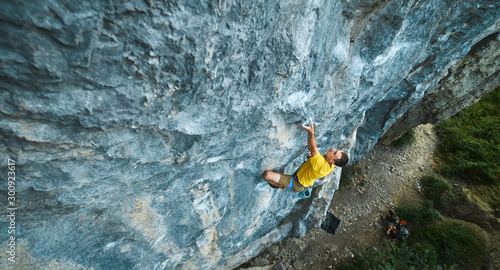 Fotografija top view of man rock climber in yellow t-shirt, climbing on a cliff, searching, reaching and gripping hold
