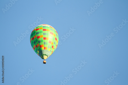 Green hot air balloon flying over the small city in a clear blue sky.