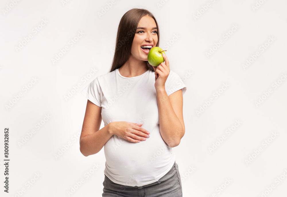Pregnant Woman Eating Apple Posing Over White Studio Background Pregnant Woman Eating Apple Posing Over White Studio Background