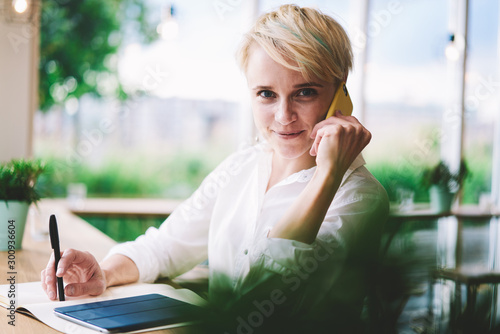 Portrait of positive woman with modern smartphone gadget making good conversation via application connected to cafeteria wifi during planning meetings with colleagues, concept of communication Free Download Portrait of positive woman with modern smartphone gadget making good conversation via application connected to cafeteria wifi during planning meetings with colleagues, concept of communication - GFXLoad