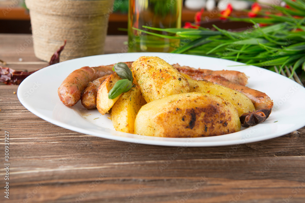 Grilled sausages with herb potatoes and ketchup, tasty summer picnic dish, sausages on skewers a dark wooden background