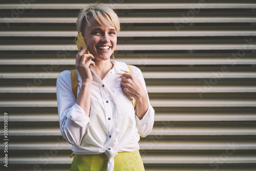 Portrait of cheerful woman in casual outfit calling to customer service for discussing details of trip, positive smiling woman using 4g connection in roaming for making smartphone conversation