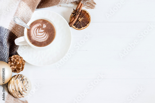 A cup of coffee with a pattern, a scarf in a cage, christmas toys, a cone on a white wooden background, flat lay. White wooden Christmas background top view
