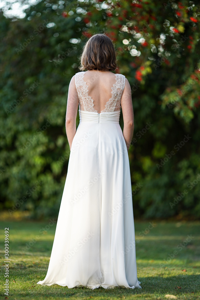 Beautiful fashionable spring bride from behind on blurred nature background. Floral bridal hairstyle.