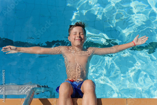  Portrait of cheerful European boy swimming in pool. He is enjoying his summer vacations. He is laying on his back with wide open hands on the water surface and smiling.