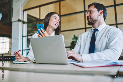 Young good looking skilled marketing experts collaborating during developing new advertising campaign using modern devices.Cheerful female and bearded male working together while sitting in office