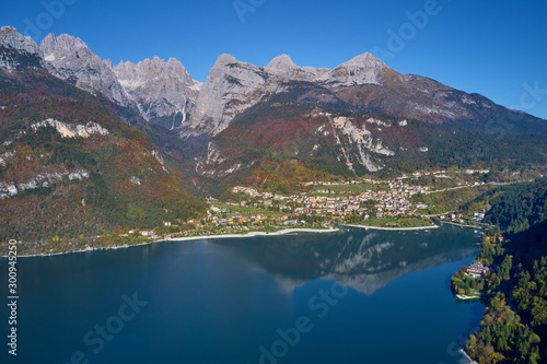 Aerial view of Lake Molveno, north of Italy in the background the city of Molveno, Alps, blue sky. Reflection of mountains in water. Autumn season. Multi-colored palette of colors