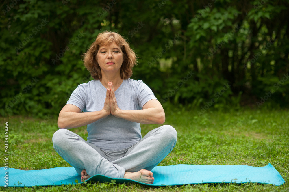 60 year old beautiful woman doing yoga in park in summer. Sports for people aged 60 year old beautiful woman doing yoga in park in summer. Sports for people aged