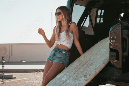 surfer girl sitting at a car with surfboard. california lifestyle