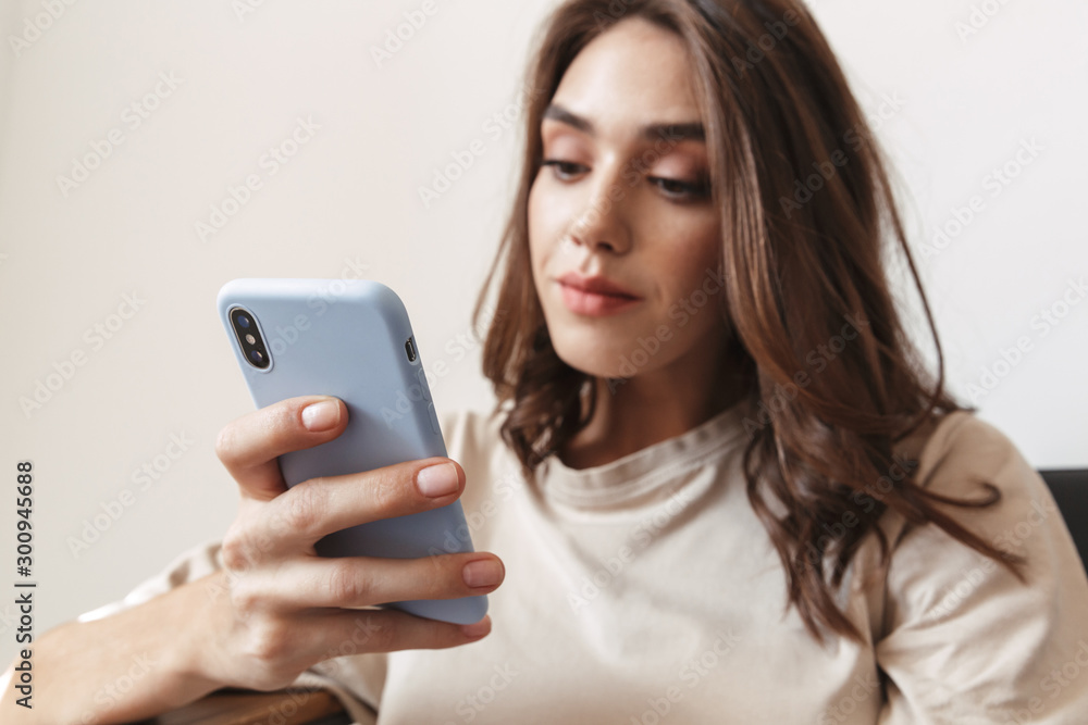 Image of woman holding smartphone and sitting on sofa in apartment Image of woman holding smartphone and sitting on sofa in apartment