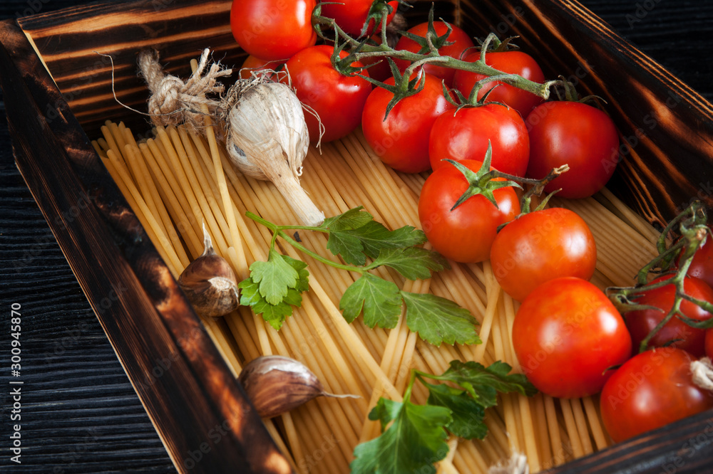 Raw pasta with cherry tomatoes garlic and parsley in wooden box Raw pasta with cherry tomatoes garlic and parsley in wooden box