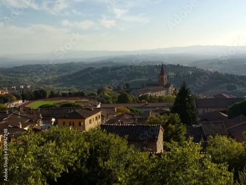 Landscape view of beautiful Perugia Italy Tuscany Europe looking across gardens valley with ancient church vineyards trees houses and mountains and fields on travel holiday in Autumn in sunshine photo