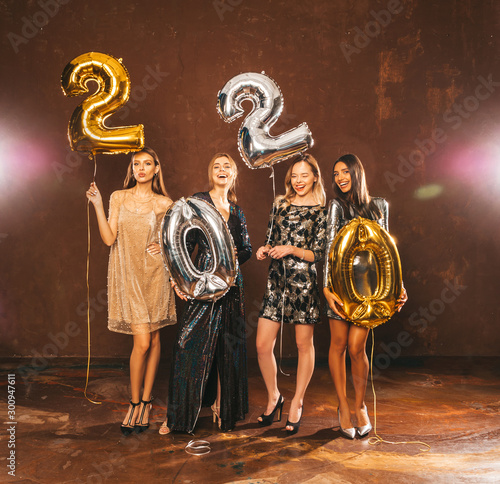 Beautiful Women Celebrating New Year.Happy Gorgeous Girls In Stylish Sexy Party Dresses Holding Gold and Silver 2020 Balloons  Having Fun At New Year s Eve Party.