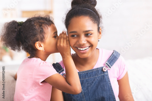 Playful african sister whispering secrets at home