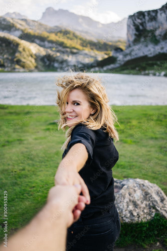 A beautiful caucasian blonde woman holds a man's hand in a mountainous landscape with lake A beautiful caucasian blonde woman holds a man's hand in a mountainous landscape with lake