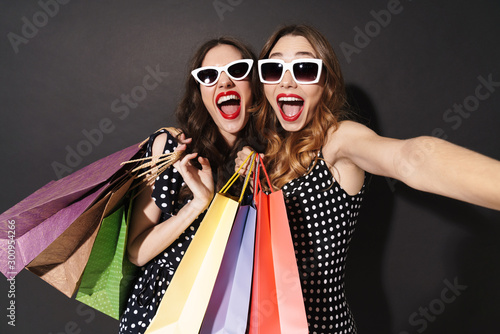 Image of girls taking selfie on cellphones and holding shopping bags