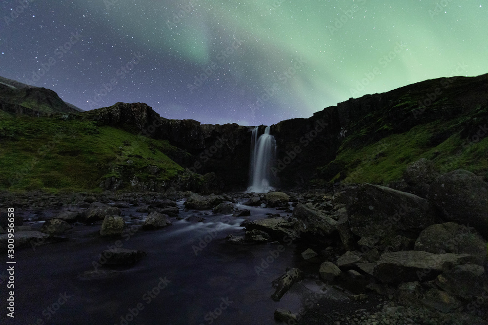Northern lights over Gufufoss waterfall, East Iceland.