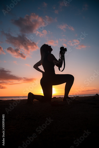 The silhouette of a female hobbyist photographer taking photos of a beautiful colorful sunset on the West Puerto Rico coast near Rincon 