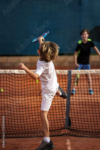 8 years old boy playing tennis with his 12 years old brother, finishing a smash movement