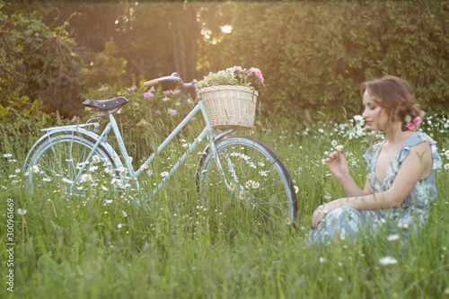the bike stands on a summer day in the field, a girl with a flower sits nearby