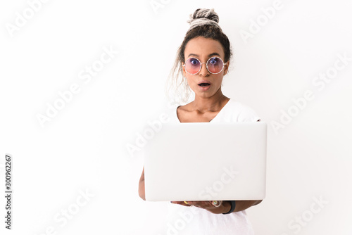 Shocked emotional young african woman with dreads posing isolated over white wall background using laptop computer.