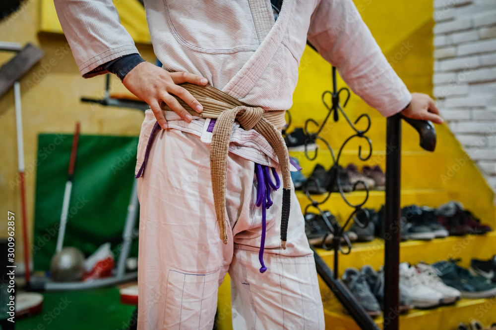 Midsection of brazilian jiu jitsu BJJ brown belt tied on the waist of athlete on the training standing at the academy wearing white gi kimono
