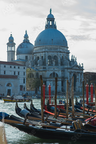 Traditional venetian gondolas by the waterfront. Several boats for travelers and tourists are covered with covers at the pier. View of the Grand Canal in Venice. Journey to Italy.