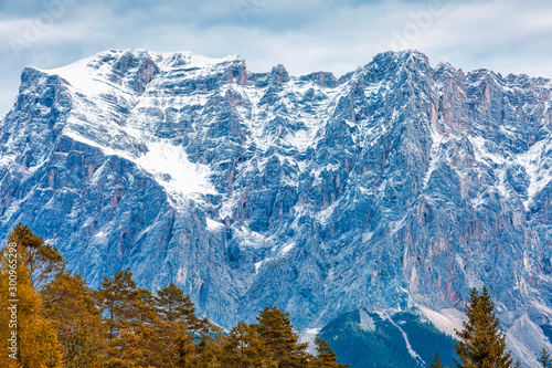 Snow-covered alpine mountains and colorful, autumn tree tops