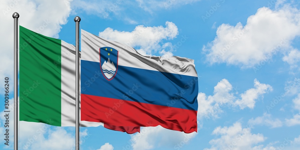Italy and Slovenia flag waving in the wind against white cloudy blue sky together. Diplomacy concept, international relations.