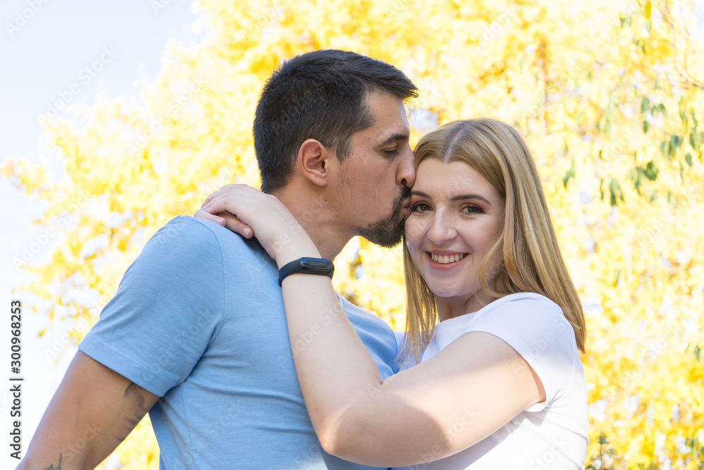Tan Husband kissing with tenderness and love the forehead of his Blond wife. Heterosexual couple embracing and hug on a intimacy date in fall. Happy couple in harmony. Tan Husband kissing with tenderness and love the forehead of his Blond wife. Heterosexual couple embracing and hug on a intimacy date in fall. Happy couple in harmony.
