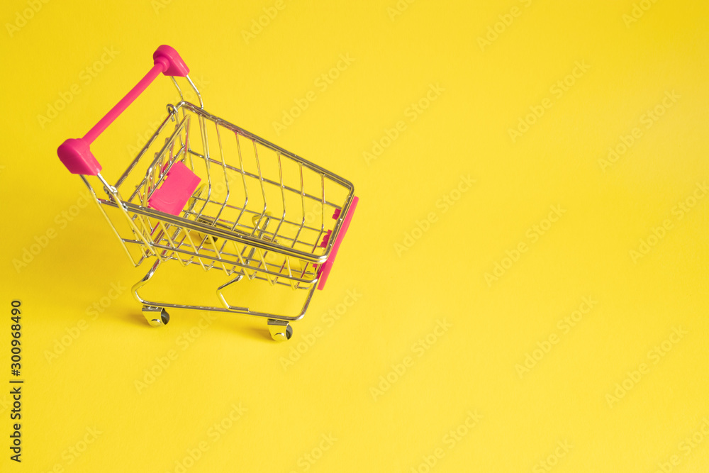 Empty shopping trolley with pink handle on yellow background. Online shopping concept. A form of electronic commerce. Empty shopping trolley with pink handle on yellow background. Online shopping concept. A form of electronic commerce.