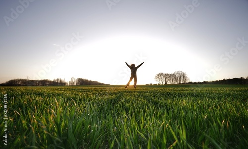 Joyful and happy girl is jumping with open arms on a green field at sunset with the sun in the background