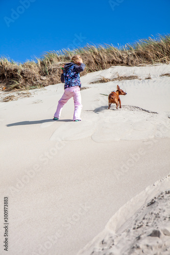Little girl climbing up dune in the summer with dog