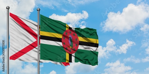 Jersey and Dominica flag waving in the wind against white cloudy blue sky together. Diplomacy concept, international relations.