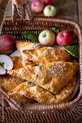 Homemade triangular pies with apples from ready-made puff pastry, in a wooden wicker basket, with fresh apples