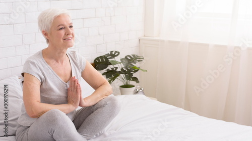 Serene senior lady meditating in Namaste pose on bed