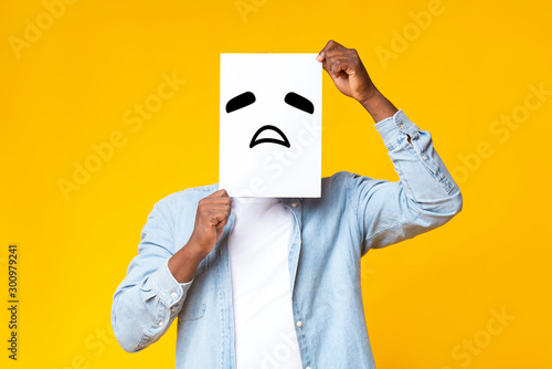 Fotografie, Obraz African american guy hiding face behind paper with sad emoticon